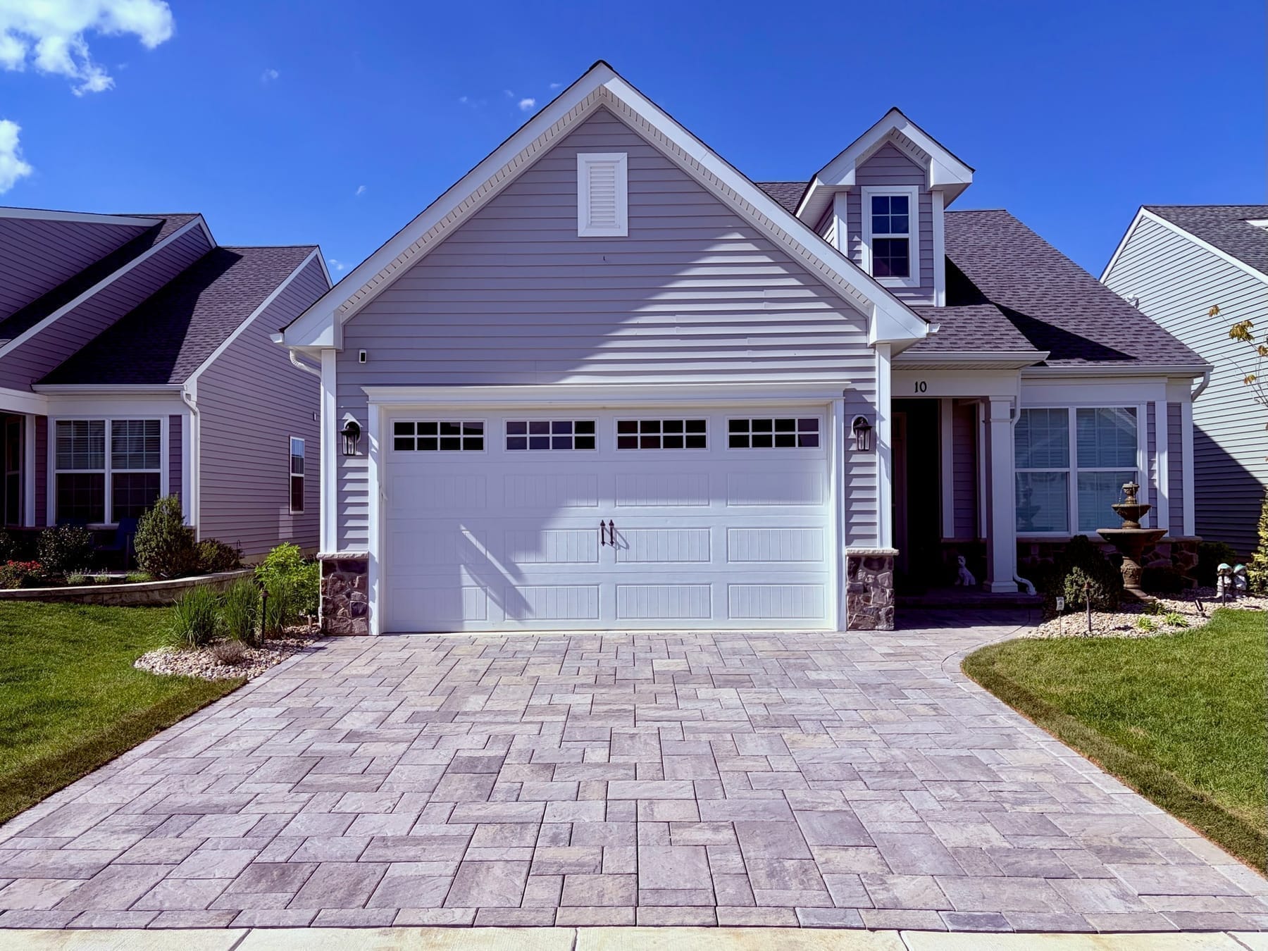 Wide tumbled paver driveway in a multi-stone pattern leading to a two-car garage on a cape-style home